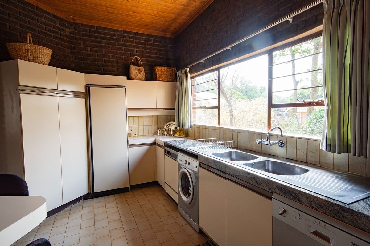 A functional kitchen featuring built-in cabinetry, a double stainless steel sink, tiled backsplash, and large windows providing natural light.