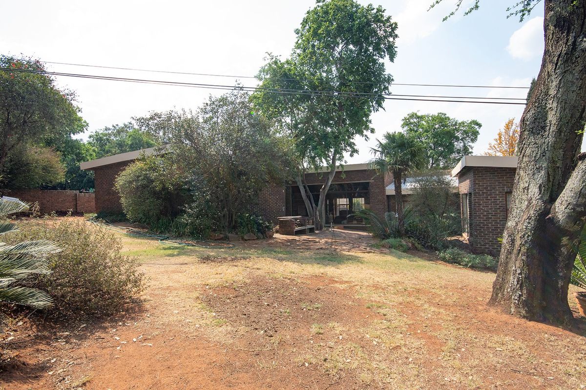 A view of the rear exterior of the brick house, featuring a paved patio area and established garden surroundings.