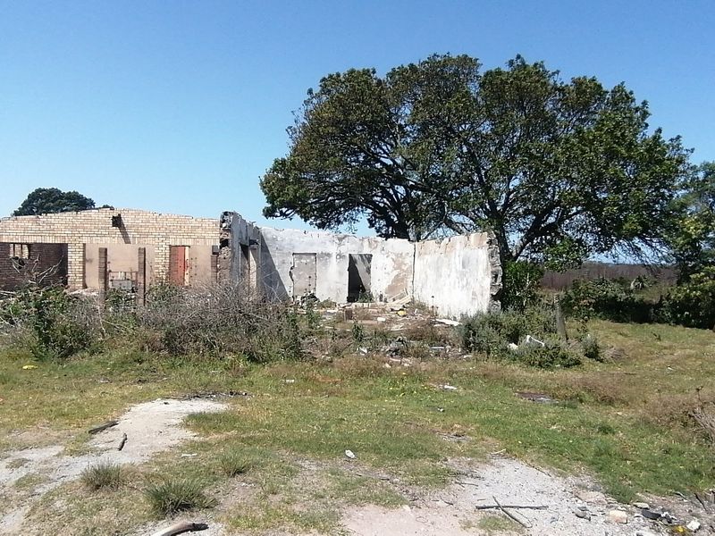 A dilapidated farm building structure showing significant deterioration, missing roof, and damaged masonry walls on a rural property.