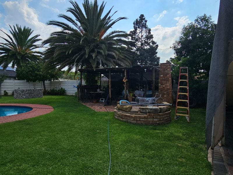 Outdoor entertainment area featuring a swimming pool, a brick fire pit, and a covered patio structure set within a landscaped garden.