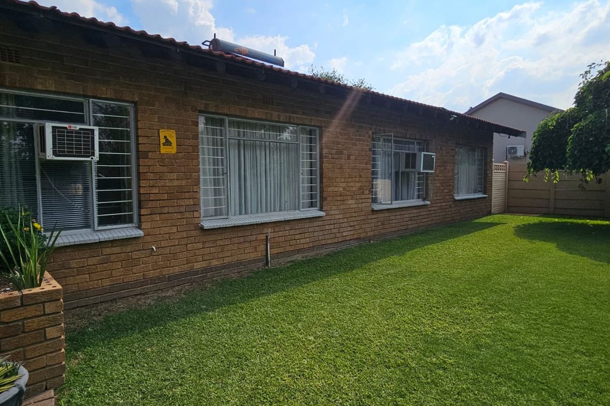 Rear view of the face brick house featuring a well-maintained lawn, tiled roof, and solar water heating system.