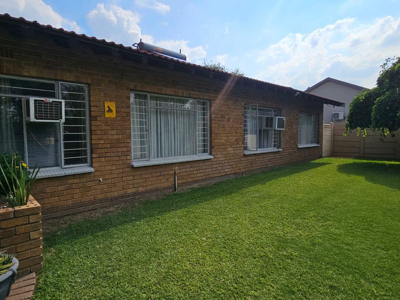 Rear view of the face brick house featuring a well-maintained lawn, tiled roof, and solar water heating system.