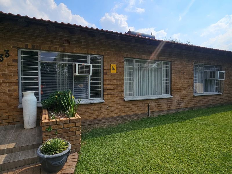 Front elevation of a face brick house featuring steel-framed windows with security bars, window-mounted air conditioning units, and a solar water heating system.