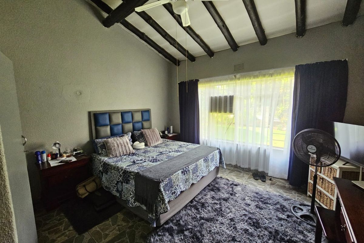 Spacious bedroom featuring exposed timber ceiling beams, tiled flooring, and a built-in window air conditioning unit, offering a rustic aesthetic.