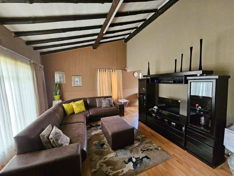 Spacious living room featuring exposed timber ceiling beams, laminate flooring, and distinctive vertical timber wall paneling, offering a warm and rustic aesthetic.