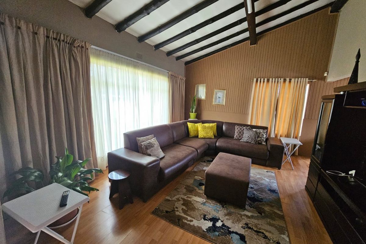 Spacious living room featuring high vaulted ceilings with exposed timber beams, wood-look flooring, and large windows providing ample natural light.