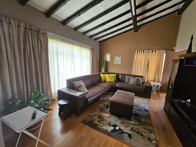 Spacious living room featuring high vaulted ceilings with exposed timber beams, wood-look flooring, and large windows providing ample natural light.