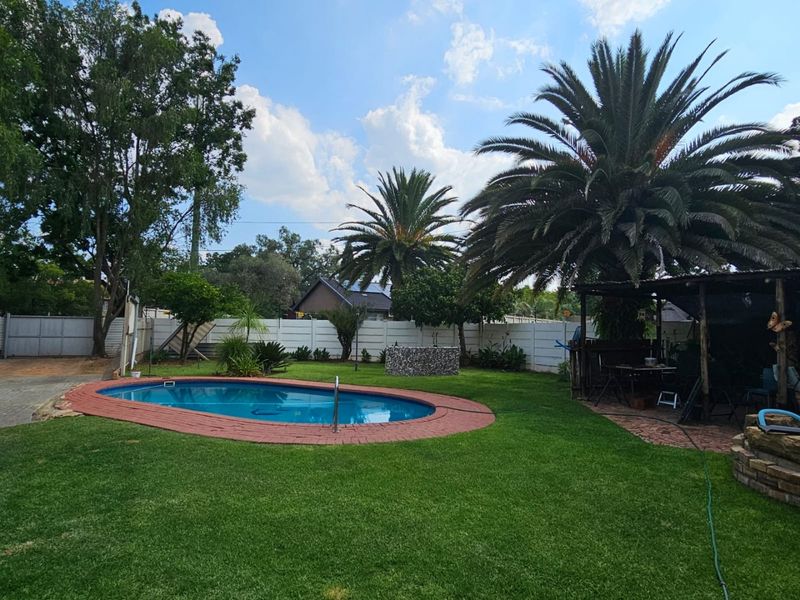 A well-maintained backyard featuring a swimming pool with brick coping, a lush lawn, and a covered patio area for outdoor entertainment.