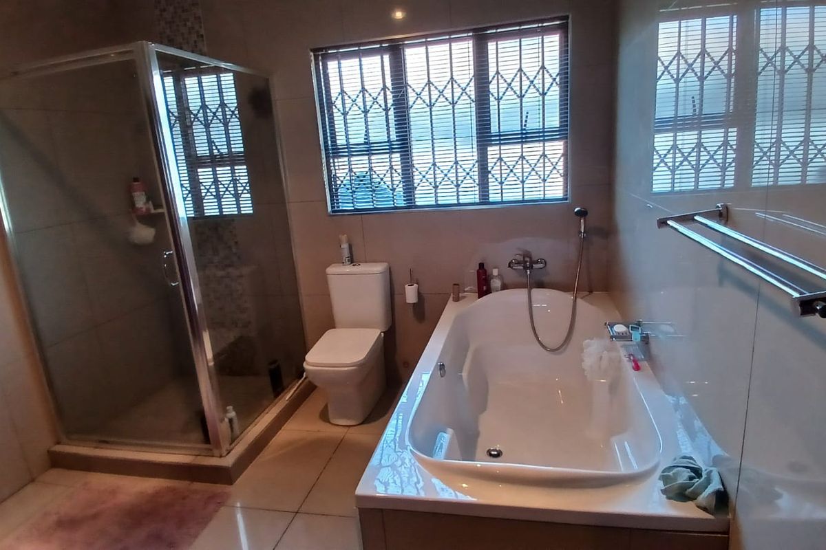 A functional bathroom featuring a glass-enclosed shower, a built-in bathtub with handheld showerhead, a toilet, and tiled walls and flooring.