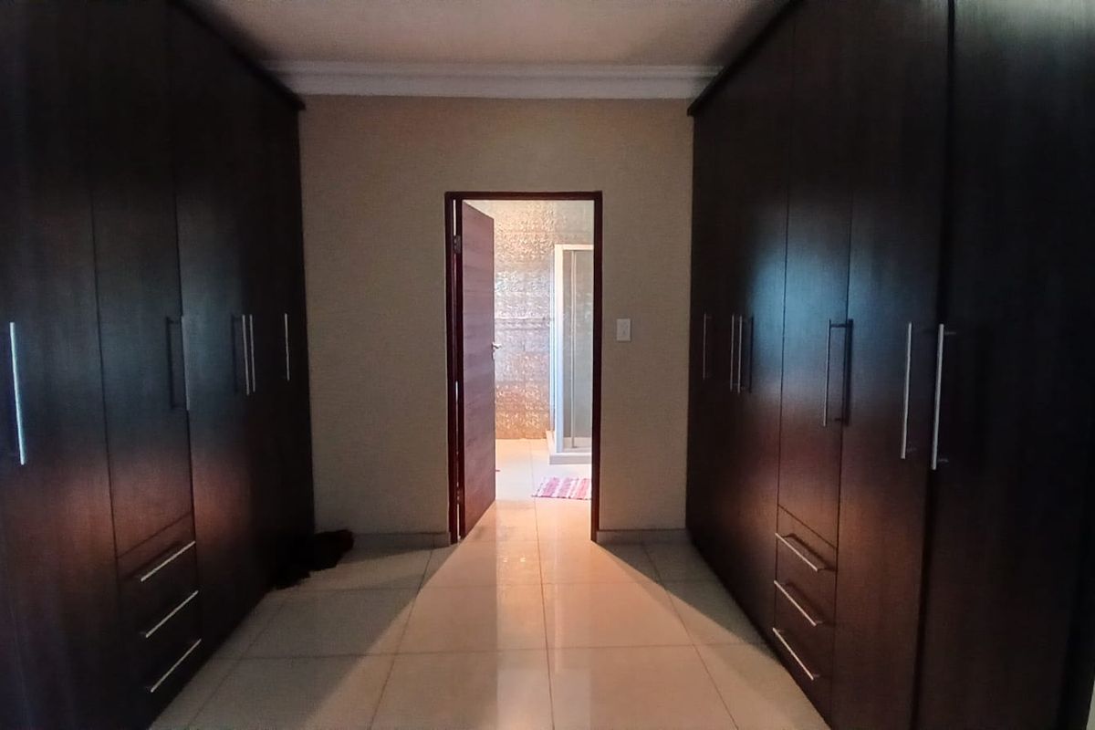A walk-in dressing area featuring extensive dark wood built-in cabinetry and tiled flooring, leading directly into an en-suite bathroom.