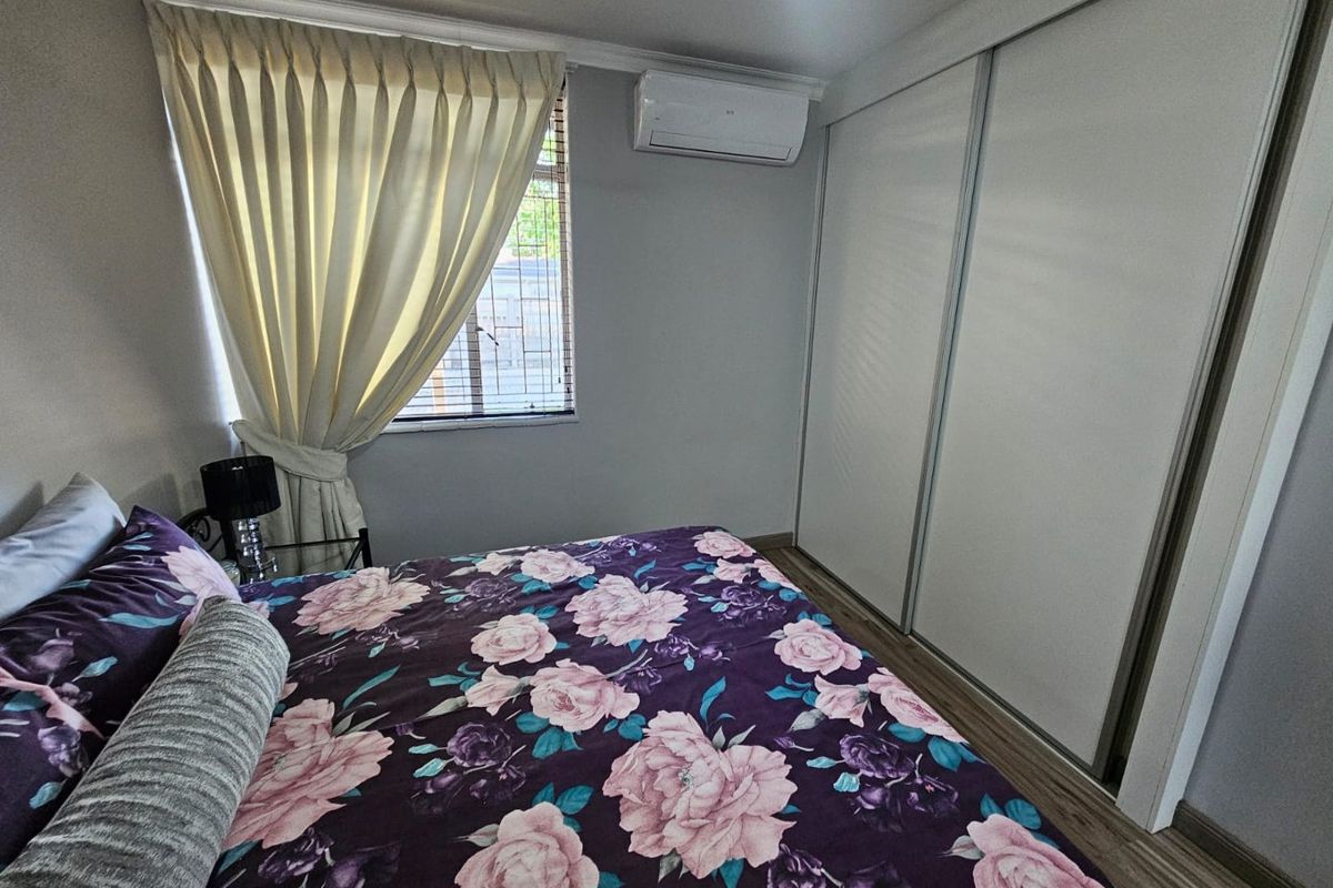 A well-maintained bedroom featuring built-in sliding door wardrobes, a wall-mounted air conditioning unit, and wood-look flooring.