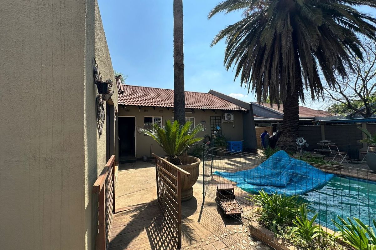 Rear exterior view featuring a swimming pool with a safety fence, paved patio area, and established palm tree.