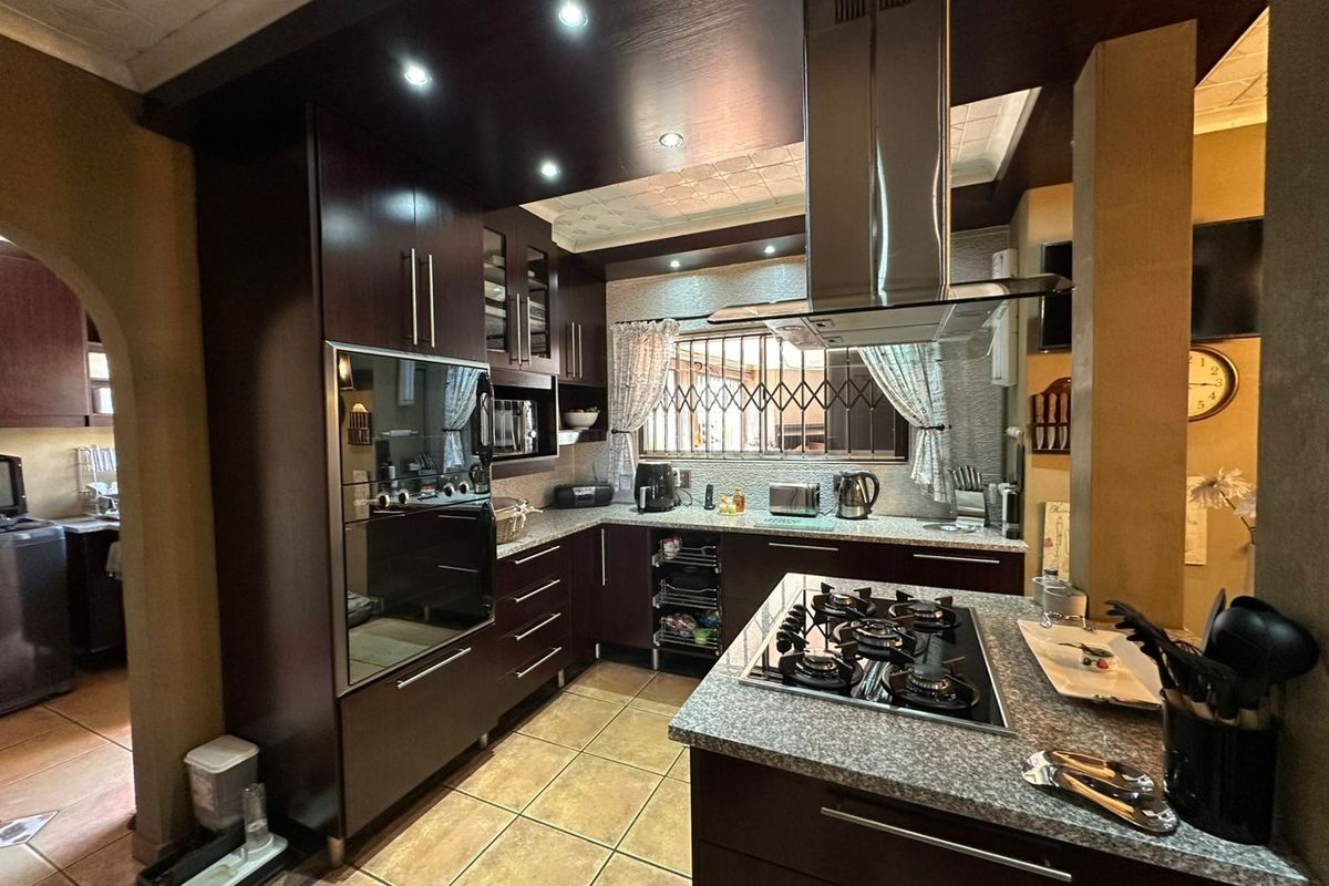 Modern kitchen featuring dark wood cabinetry, granite countertops, a central island with a gas hob, and a stainless steel extractor fan.