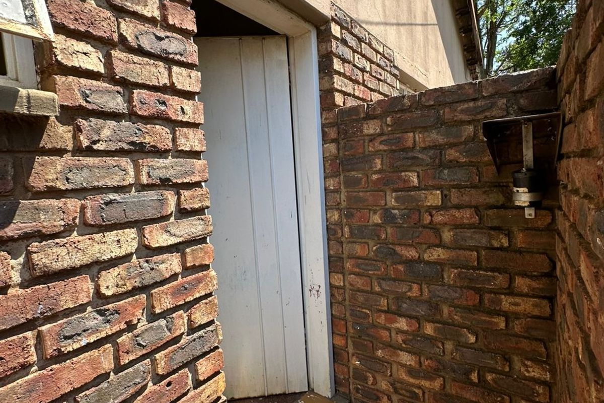 Exterior view of a side entrance featuring exposed brick walls, a concrete threshold, and a wall-mounted outdoor light fixture.