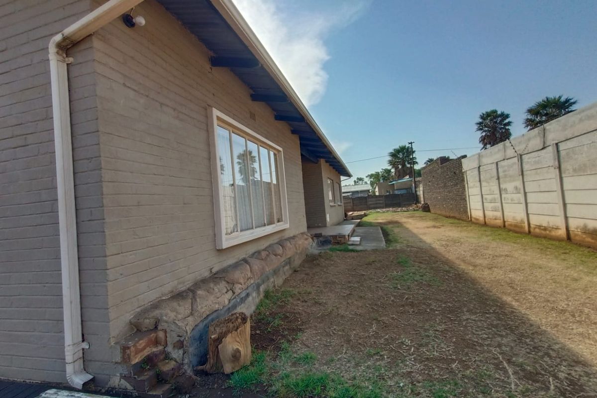 Side exterior view of the house featuring brick walls, a stone foundation base, and a large window, set against a fenced yard.
