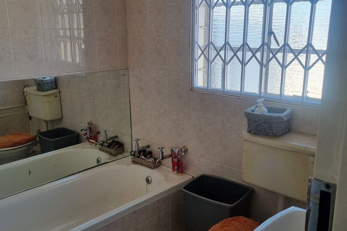 A functional bathroom featuring a built-in bathtub, toilet, and basin with tiled walls and a security-barred window.