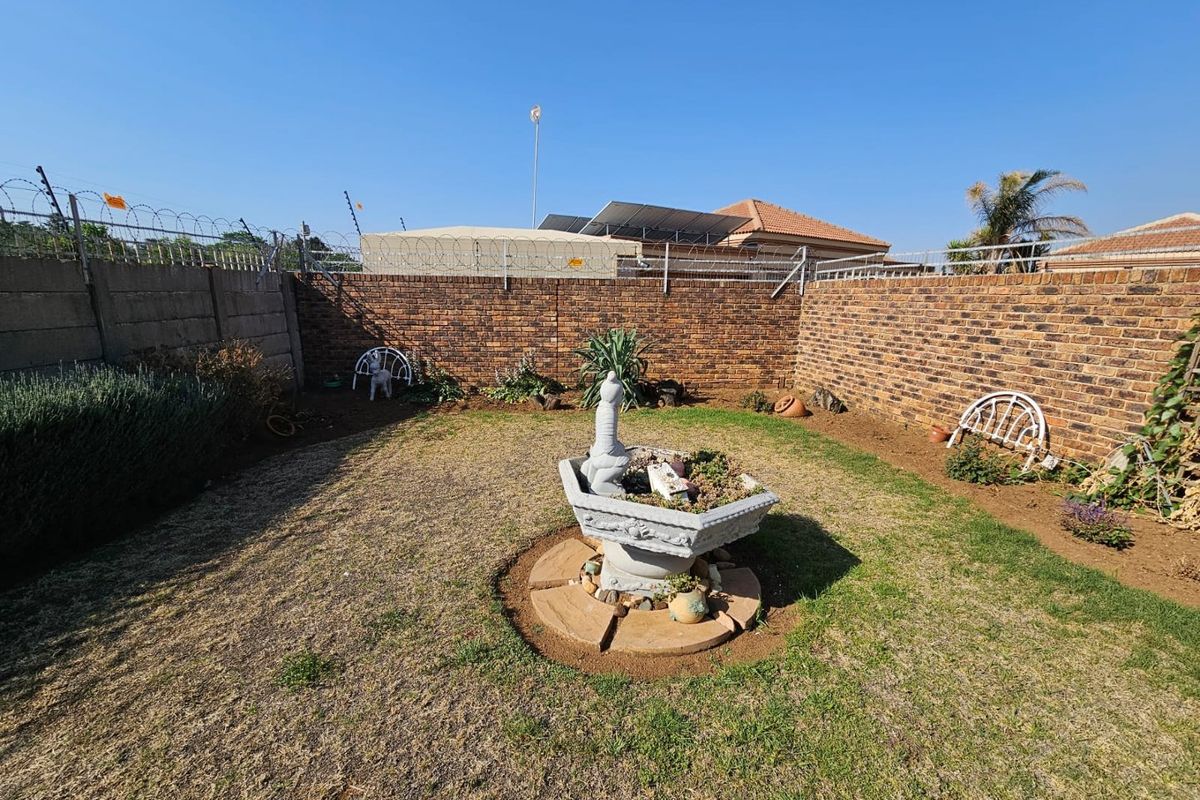A private rear garden featuring a brick boundary wall with security fencing and a central stone water feature.