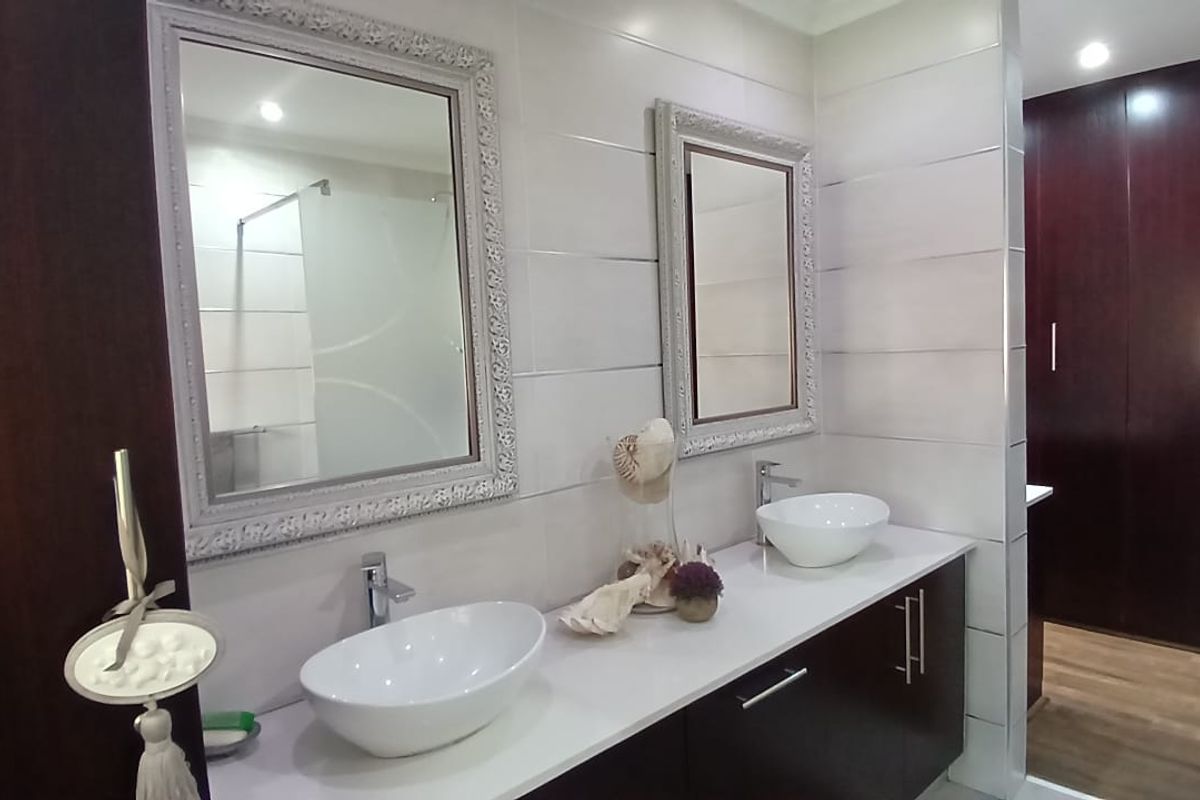 Modern bathroom featuring a double vanity with vessel sinks, sleek dark cabinetry, and large framed mirrors, adjacent to a walk-in closet area.