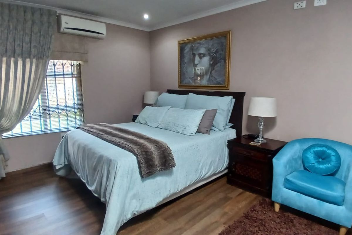 A well-maintained bedroom featuring wood-look flooring, a wall-mounted air conditioning unit, and a window with fitted security bars.