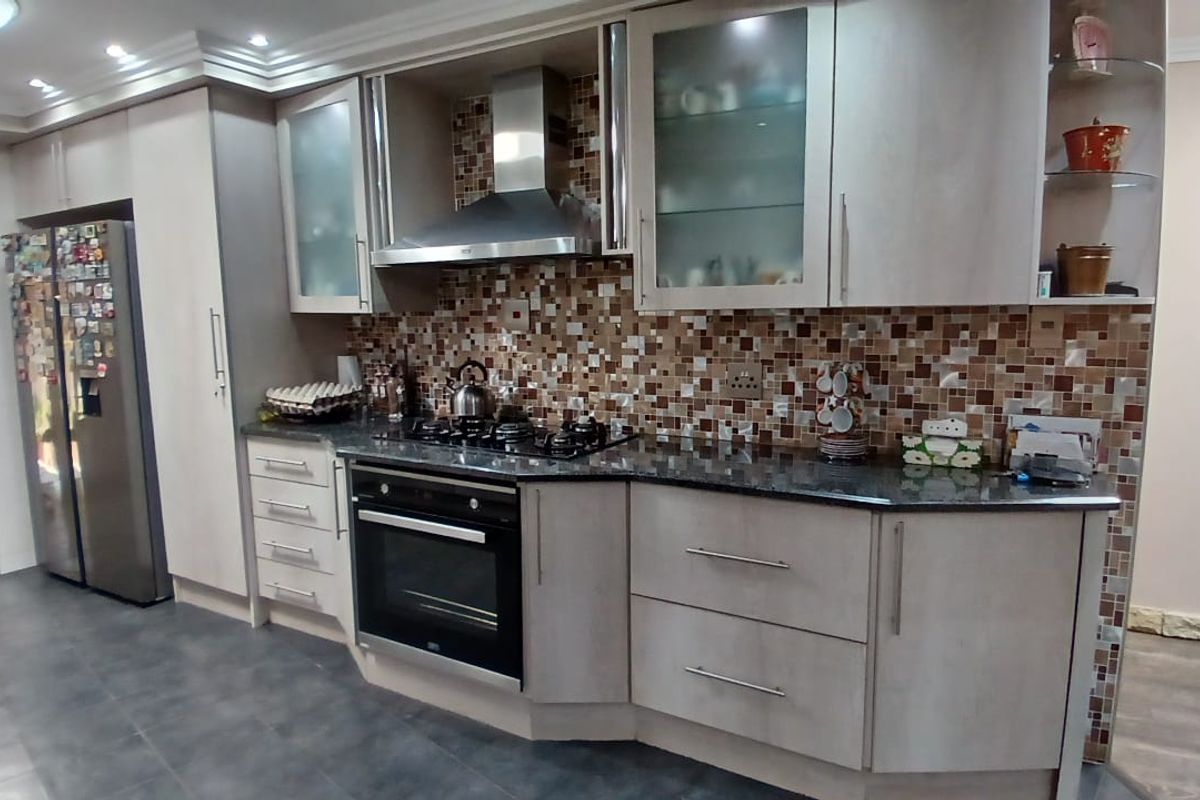 A functional kitchen featuring light-toned cabinetry, a mosaic tile backsplash, granite countertops, a built-in oven, and a stainless steel extractor fan.