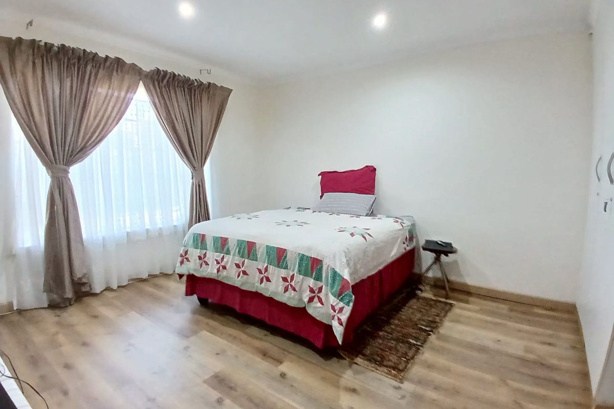 A well-maintained bedroom featuring modern wood-look laminate flooring, recessed ceiling lighting, and large windows with curtain tracks.