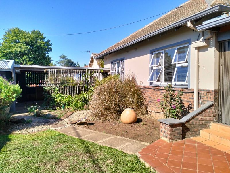 Rear exterior view of the house featuring a tiled patio, brick facade, casement windows, and a paved garden walkway leading to a covered carport.