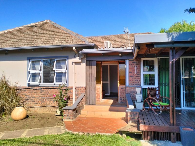Rear view of the house featuring a terracotta tiled patio, wooden deck, and brick facade with access through a sliding door.