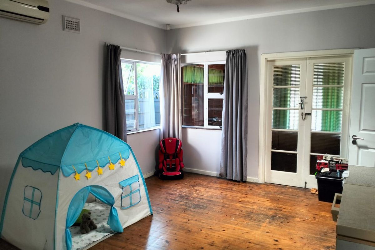A bedroom featuring original timber flooring, split-system air conditioning, and classic french doors leading to an adjacent space.