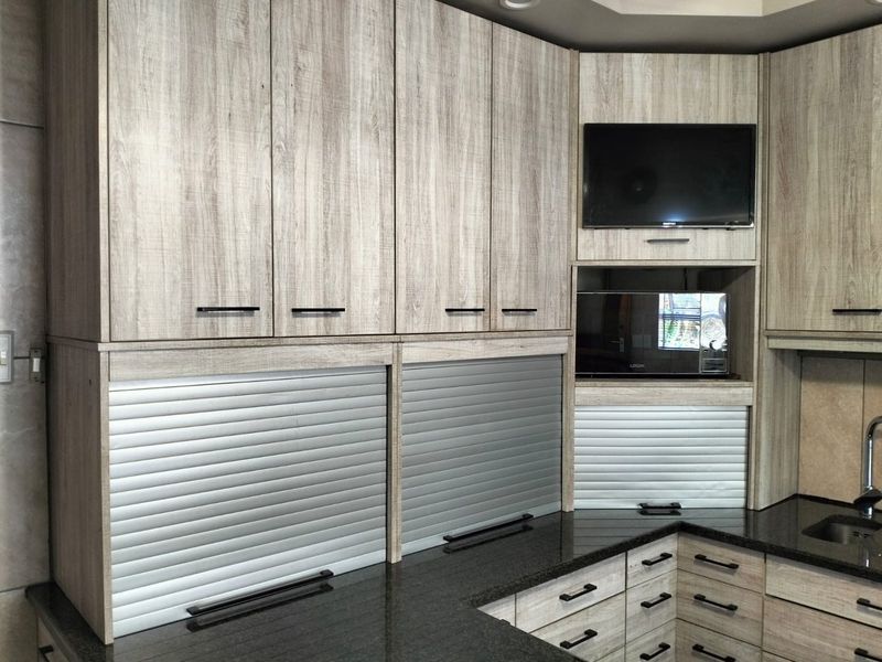 Modern kitchen featuring light wood-grain cabinetry, dark granite countertops, integrated appliance garages, and a built-in microwave.