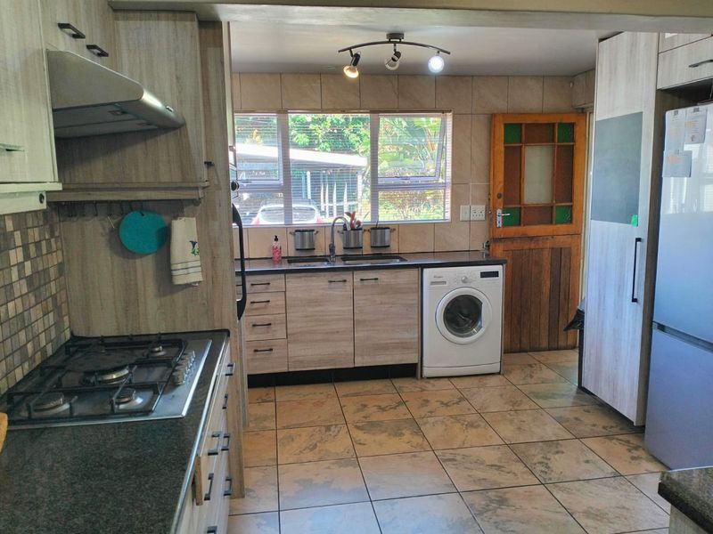 Functional kitchen featuring wood-look cabinetry, gas hob, extractor fan, tiled backsplash, and integrated laundry space with direct exterior access.