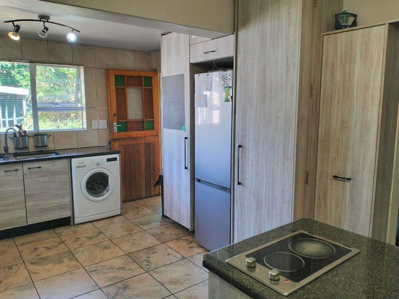 Functional kitchen featuring light wood-look cabinetry, dark countertops, integrated electric hob, and tiled flooring with direct access to the exterior.
