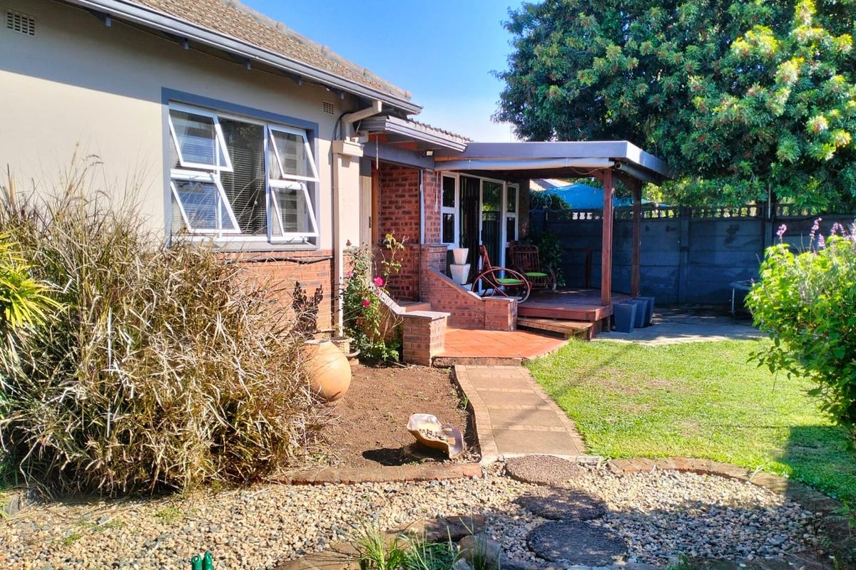 Rear view of the property featuring a covered timber patio, brick and plaster facade, and a landscaped garden with a paved walkway.