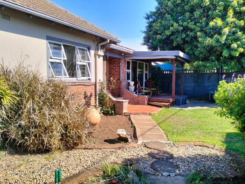 Rear view of the property featuring a covered timber patio, brick and plaster facade, and a landscaped garden with a paved walkway.