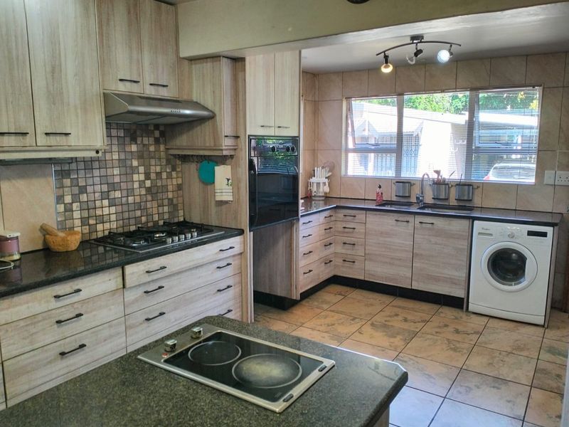 A functional kitchen featuring light wood-grain cabinetry, granite countertops, dual hobs, built-in oven, and tiled finishes with ample storage space.