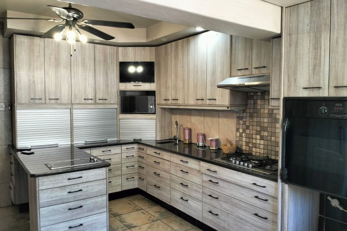 Modern kitchen featuring light wood-grain cabinetry, granite countertops, built-in oven, gas hob, extractor fan, and tiled flooring.