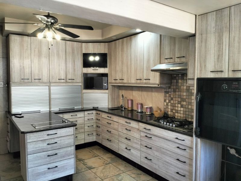 Modern kitchen featuring light wood-grain cabinetry, granite countertops, built-in oven, gas hob, extractor fan, and tiled flooring.
