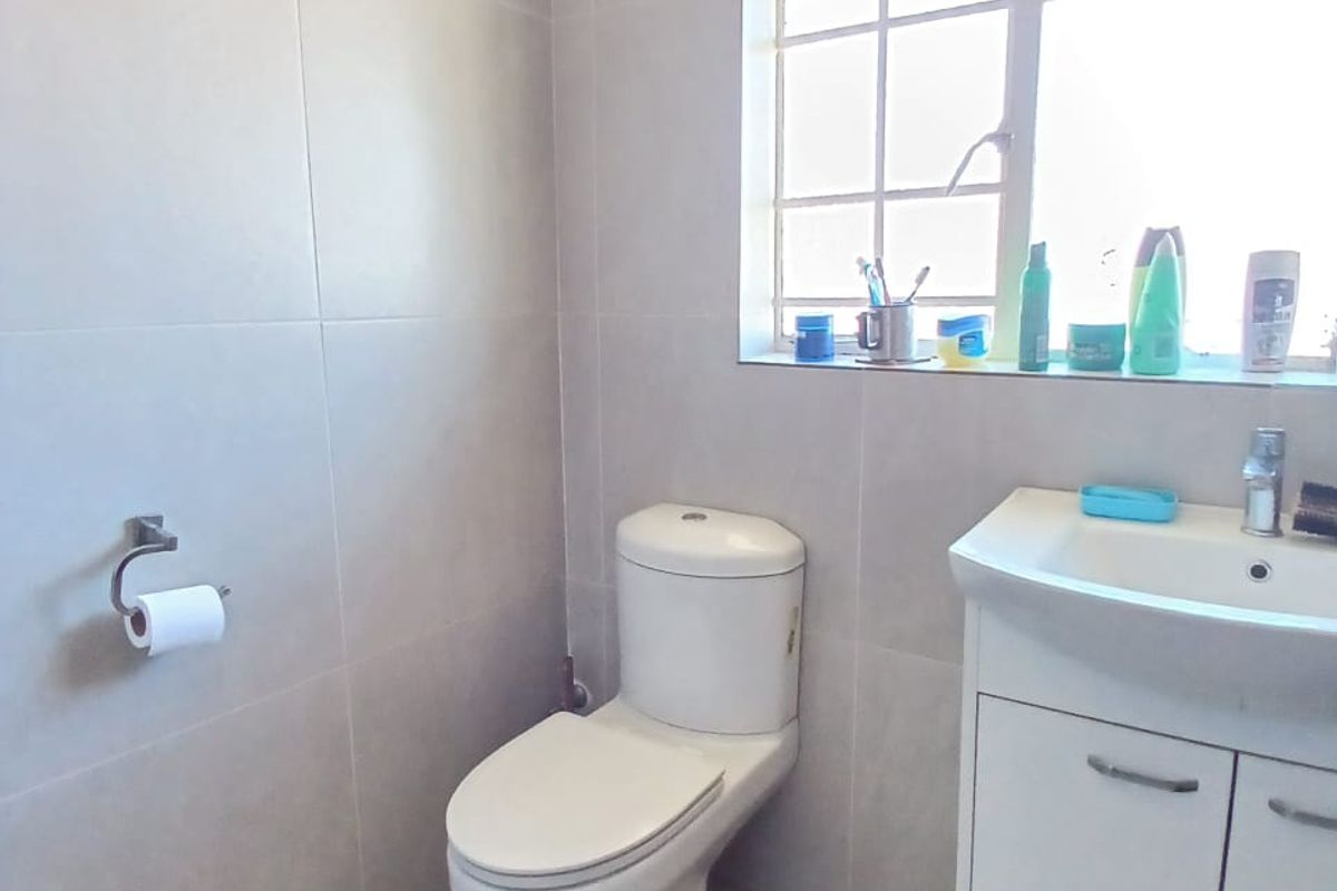 A functional bathroom featuring a modern toilet, a vanity basin with storage cabinetry, and neutral wall and floor tiling.