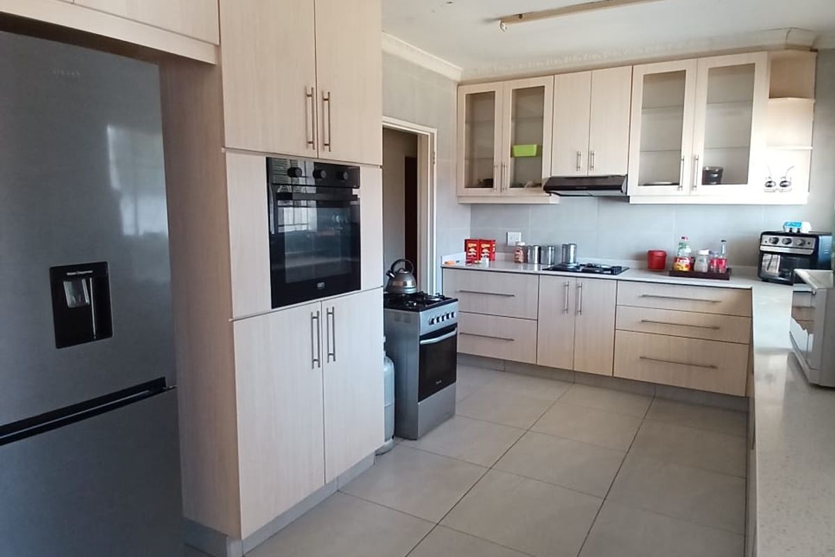 A functional kitchen featuring light wood cabinetry, built-in oven, gas hob, extractor fan, and large format floor tiles.