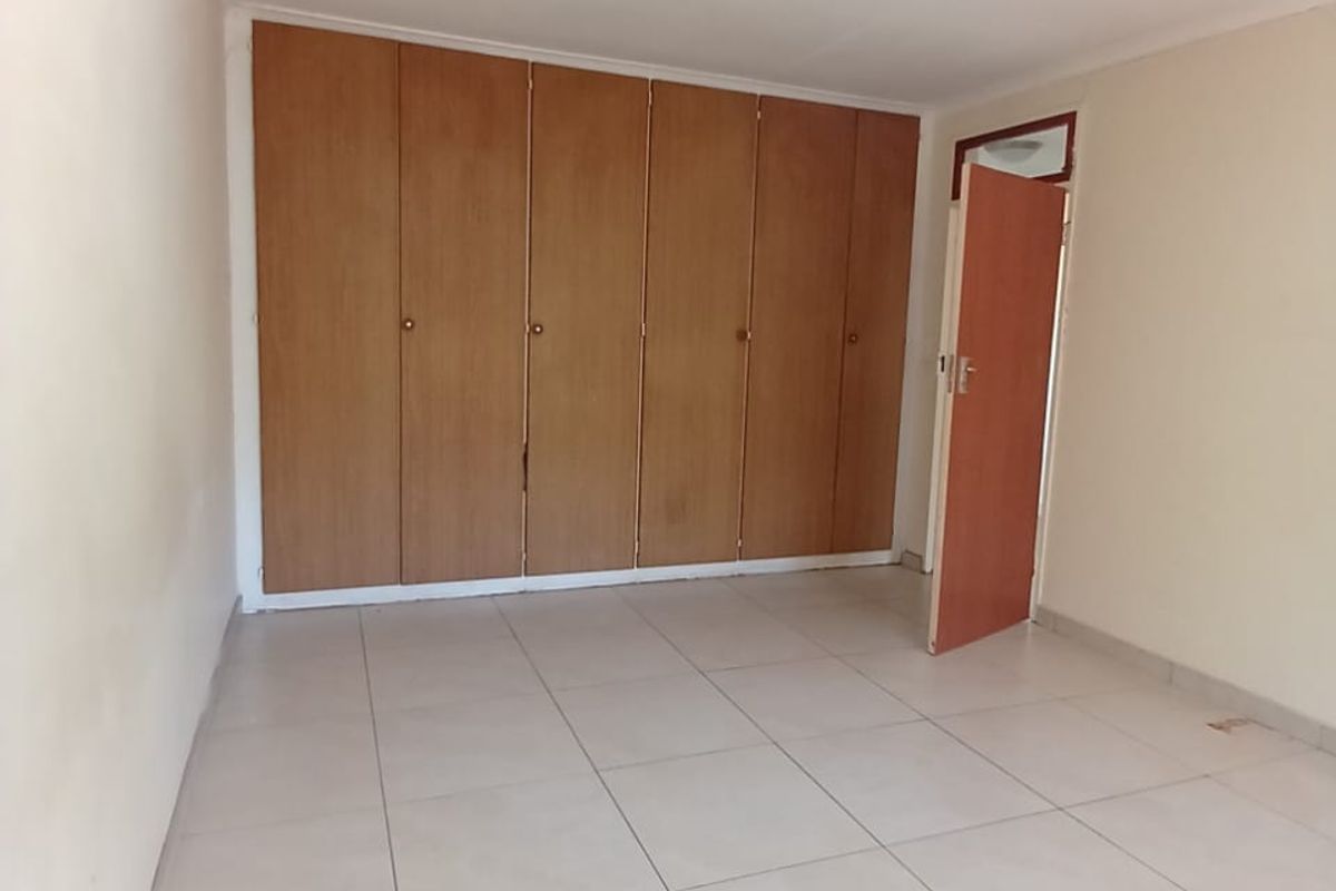 A clean, empty bedroom featuring neutral floor tiles and built-in wooden cupboards.