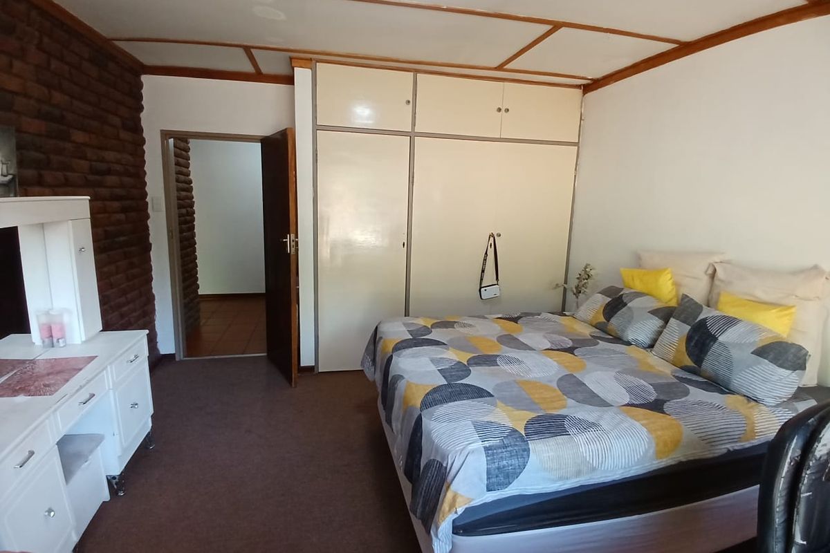 A bedroom featuring built-in cupboards, a distinctive exposed brick feature wall, and direct access to an adjoining hallway.