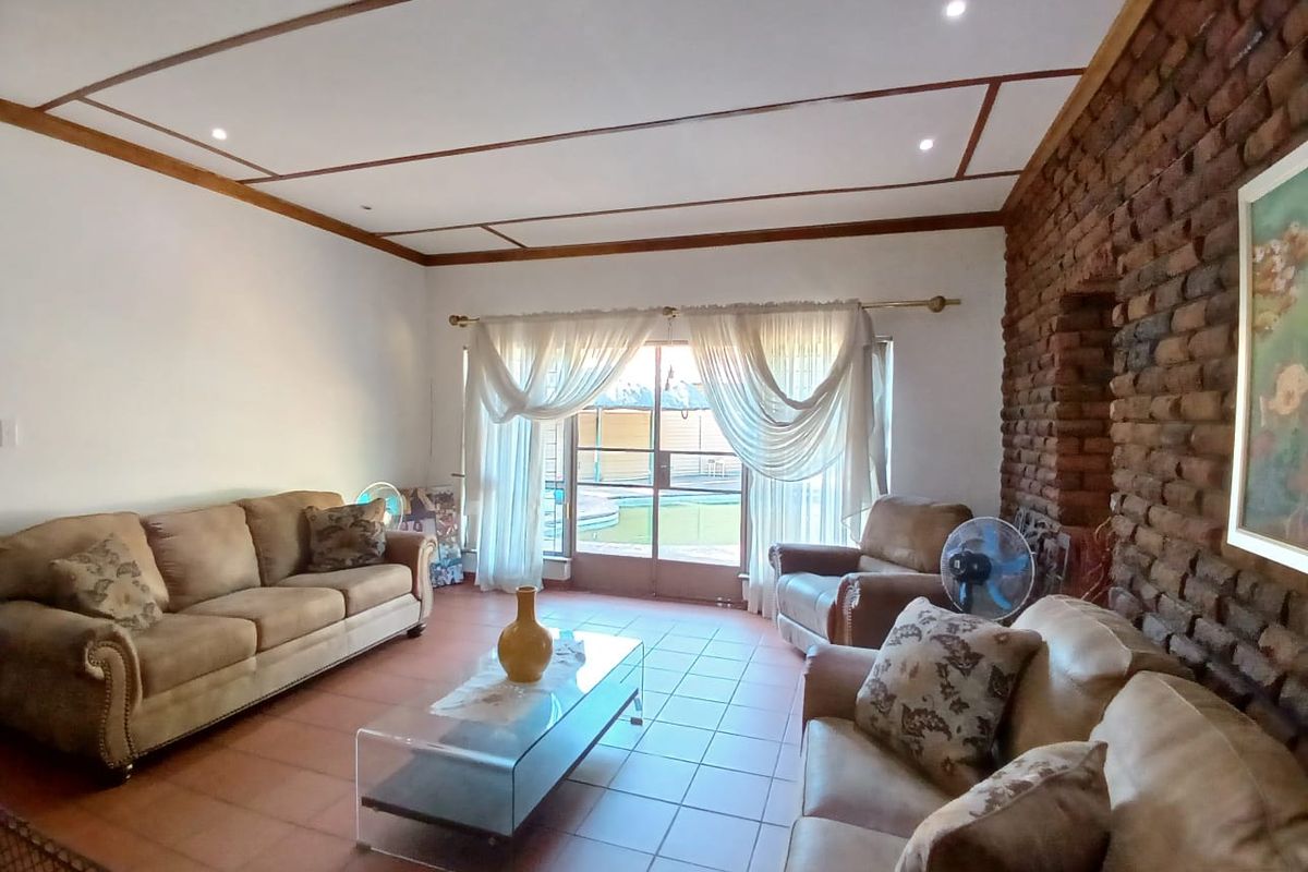 Spacious living room featuring a prominent exposed brick feature wall, tiled flooring, and sliding glass doors providing access to the outdoor pool area.