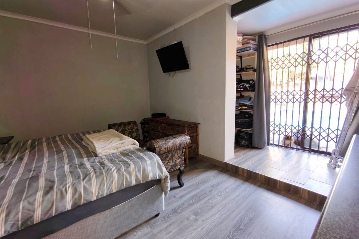 Bedroom featuring wood-look laminate flooring, a ceiling fan, and a raised alcove area with security gate access to the exterior.