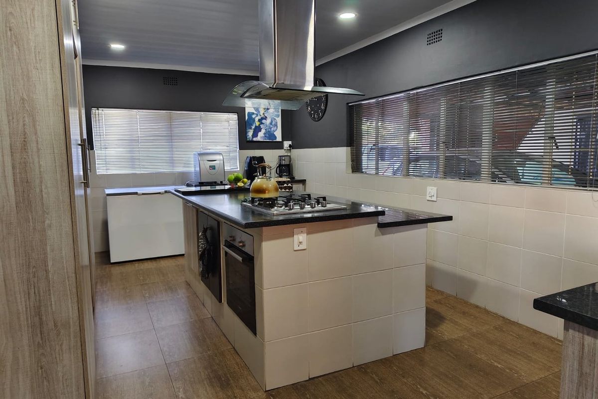 Modern kitchen featuring a central island with a built-in gas hob, oven, and stainless steel extractor fan, complemented by tiled flooring and dark accent walls.