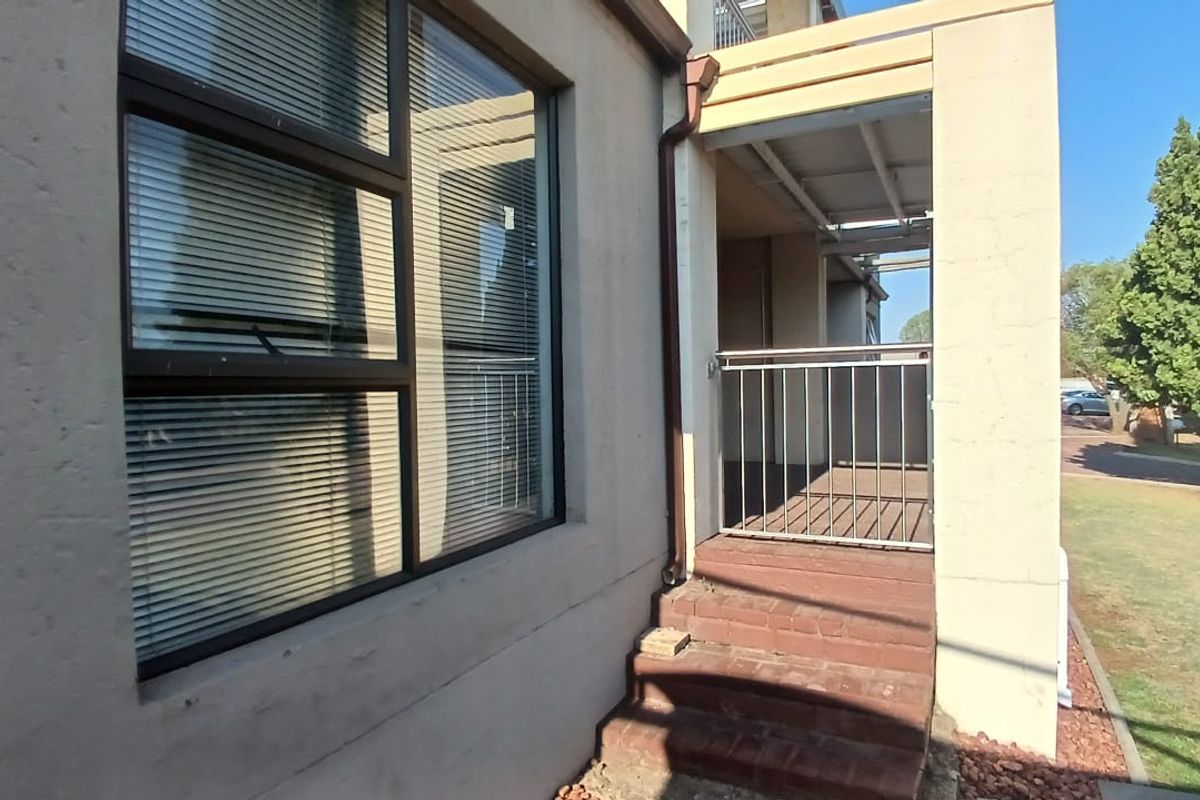 Exterior view of a flat entrance featuring a small brick staircase, metal security railing, and a covered patio area with large windows.
