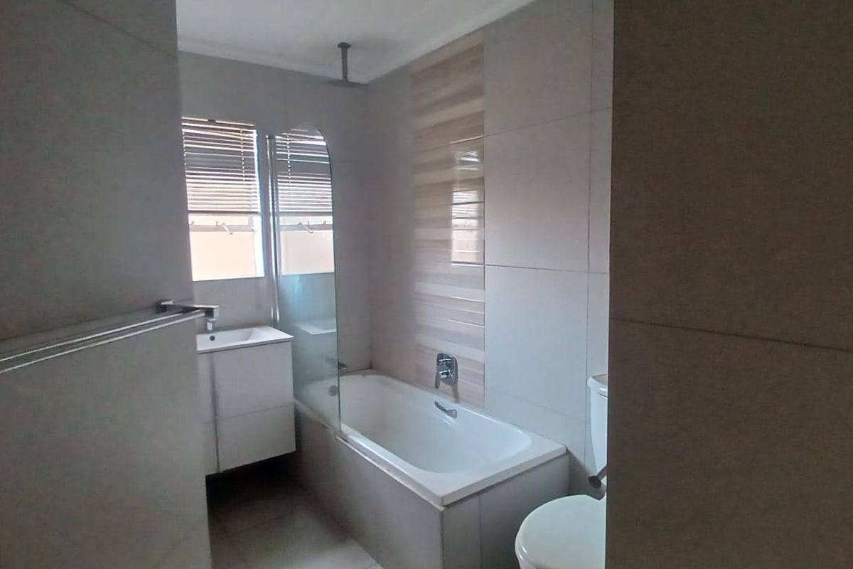 A modern bathroom featuring a built-in bathtub with a glass shower screen, a vanity basin, and neutral wall tiling.