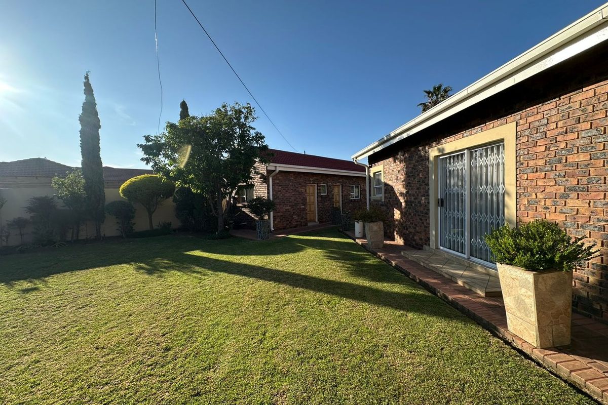 A well-maintained rear garden featuring a brick-faced exterior, a paved patio area, and a secondary outbuilding structure.