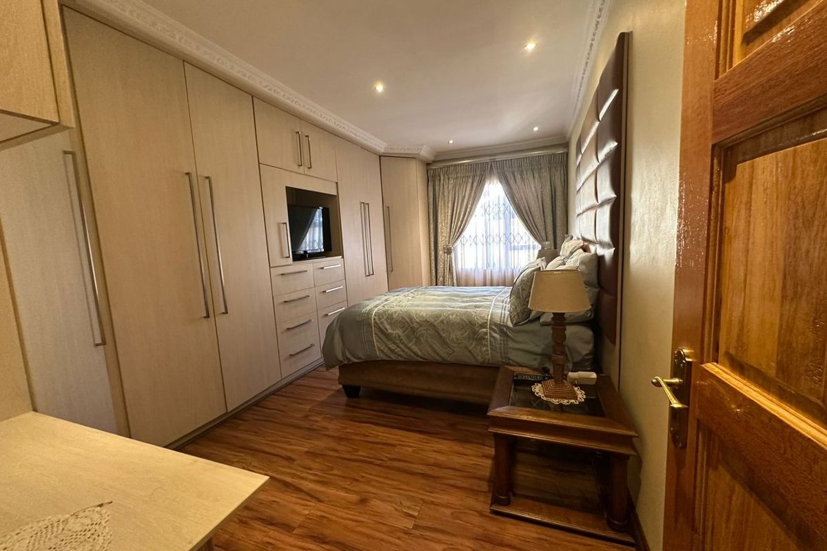 A well-maintained bedroom featuring extensive built-in cabinetry, laminate wood flooring, decorative ceiling cornices, and a padded headboard wall feature.