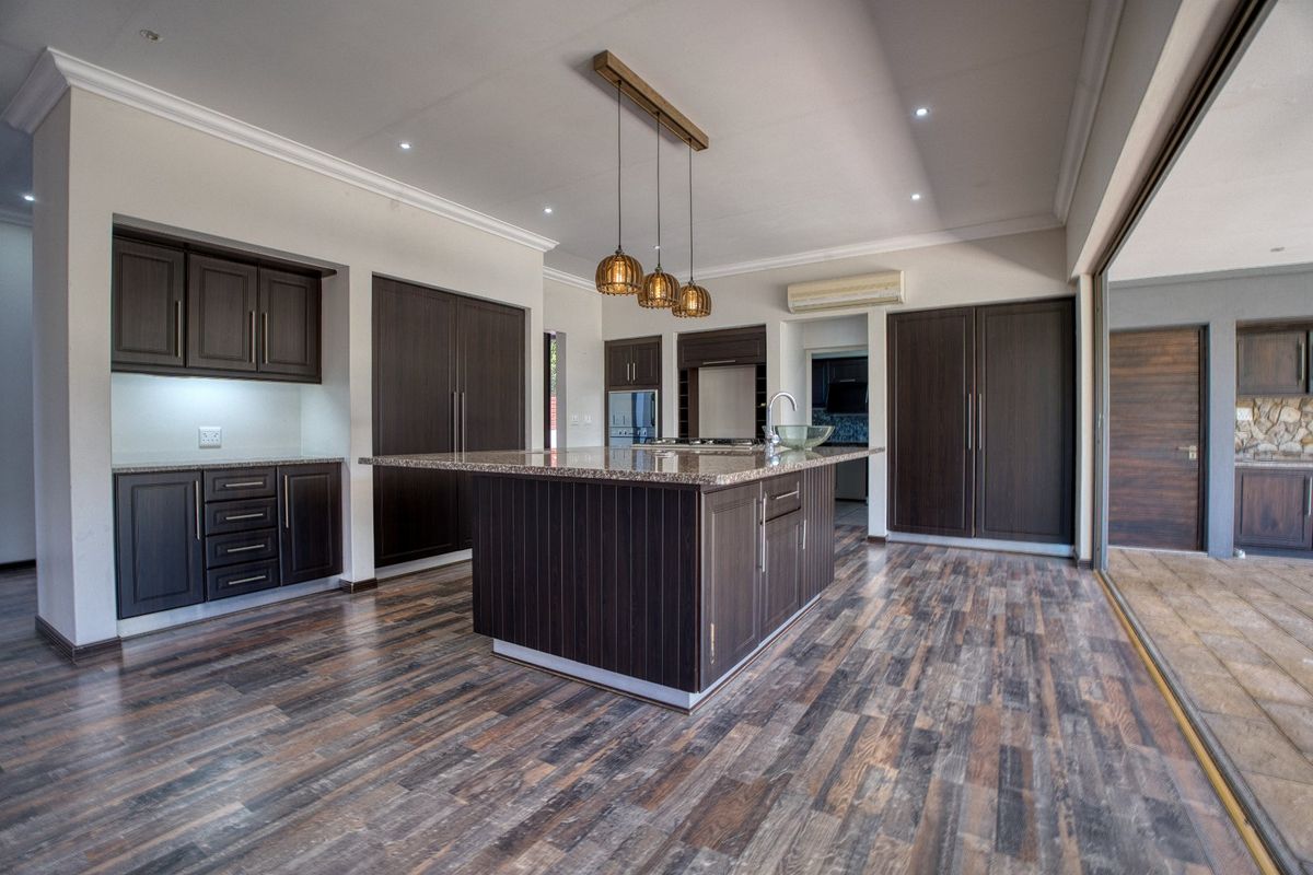 Spacious modern kitchen featuring dark wood cabinetry, a large central island with granite countertops, and seamless access to the outdoor patio area.
