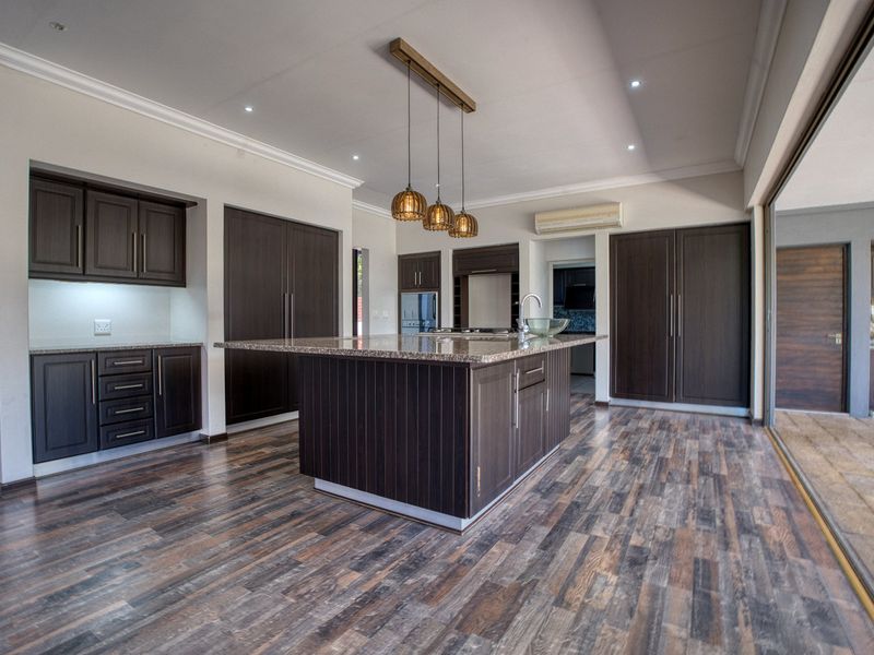 Spacious modern kitchen featuring dark wood cabinetry, a large central island with granite countertops, and seamless access to the outdoor patio area.