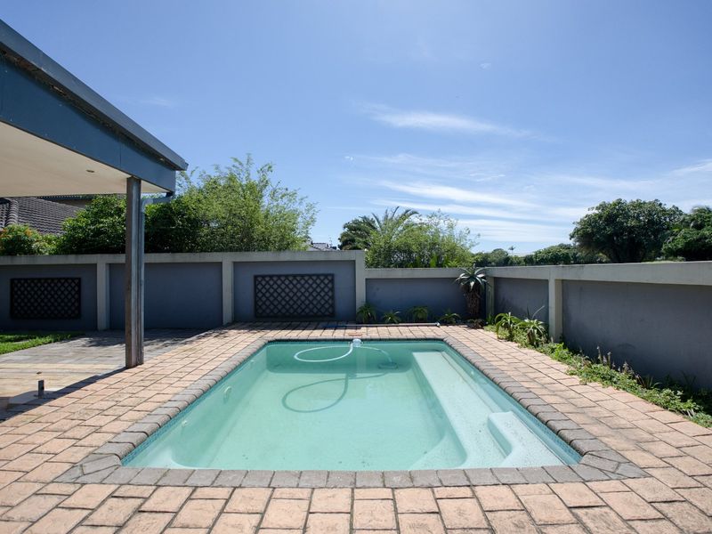 Outdoor pool area featuring a paved surround, boundary wall, and an adjacent covered patio space.